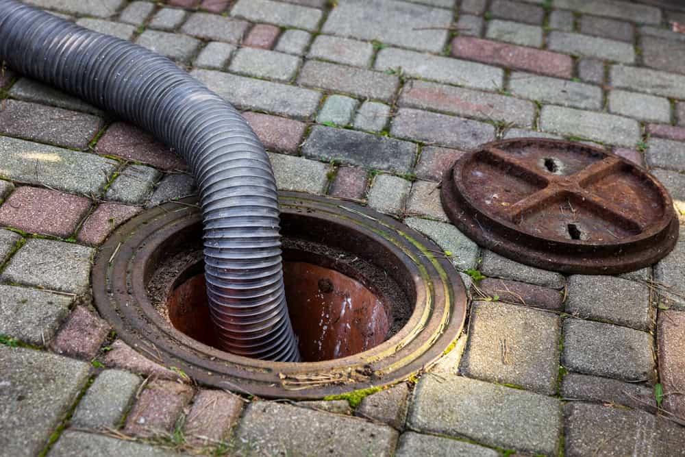 Flexible sewer drain pipe inserted into a manhole on brick pavement for septic system or cesspool maintenance.